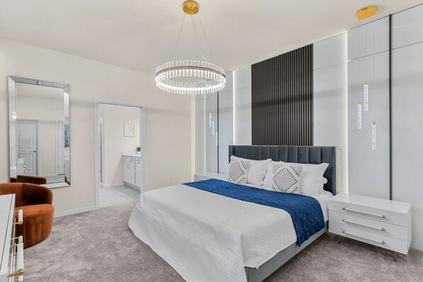 A modern bedroom with a large bed, a bedside table, a wardrobe, and a chandelier.
