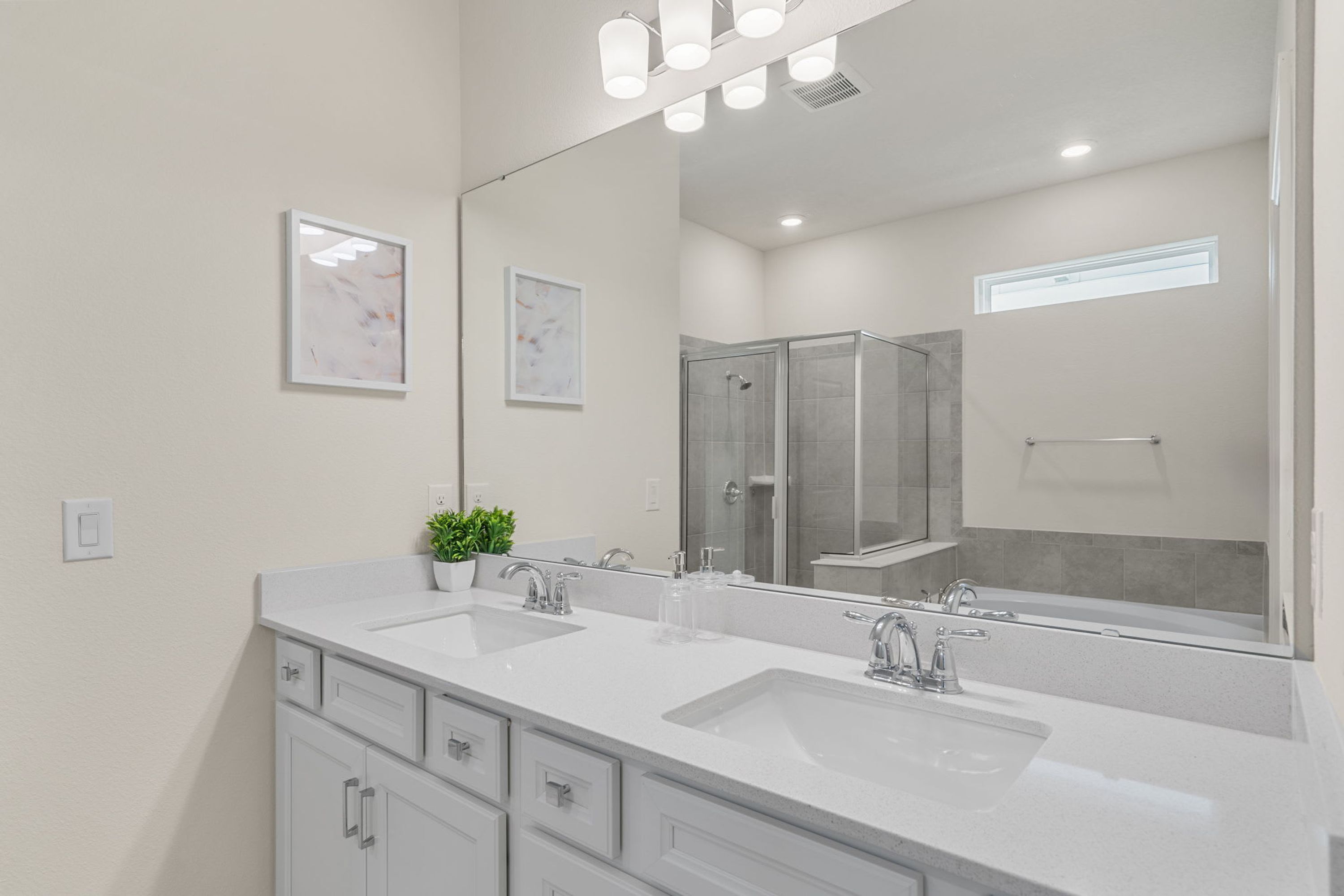 A modern bathroom with two sinks, a large mirror, and a shower area.