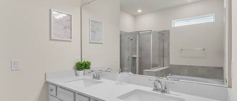 A modern bathroom with two sinks, a large mirror, and a shower area.