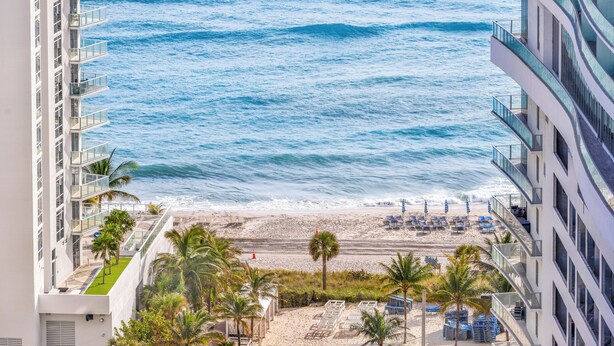 A beachfront hotel with a view of the ocean, a sandy beach, and palm trees.