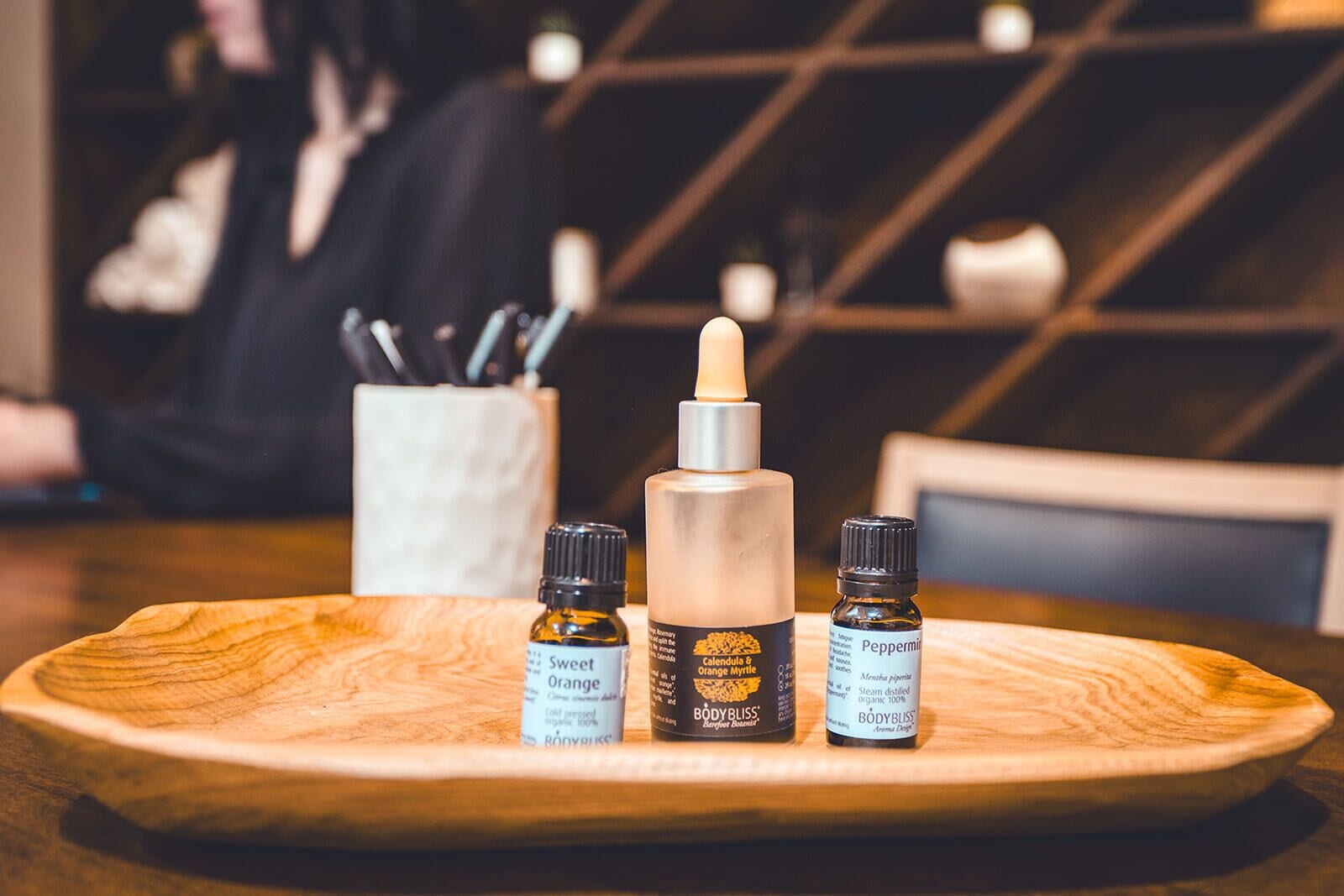 A wooden tray with three bottles of essential oils and a dropper on a table.