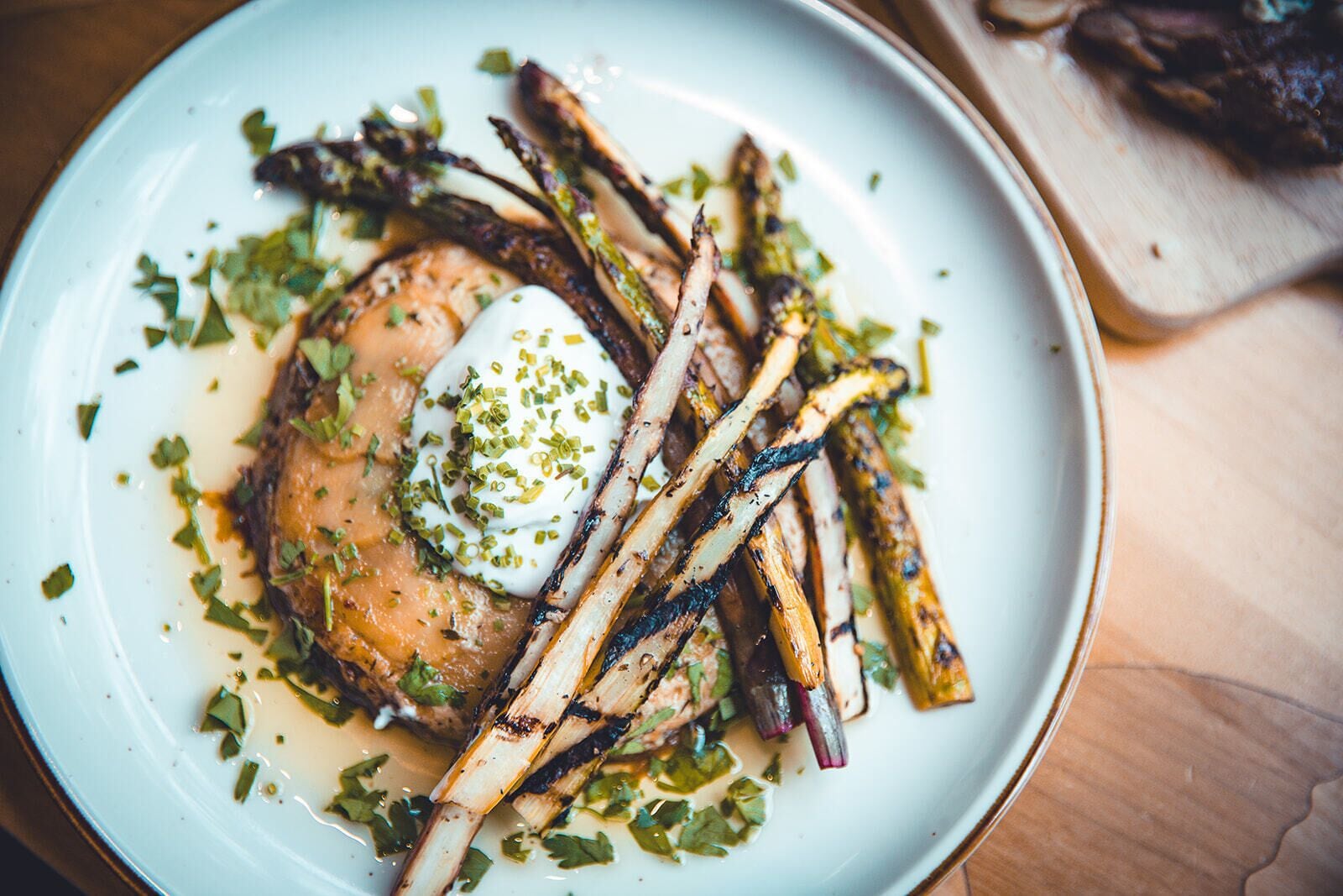 A plate with grilled asparagus, a poached egg, and a sauce, garnished with chopped herbs.