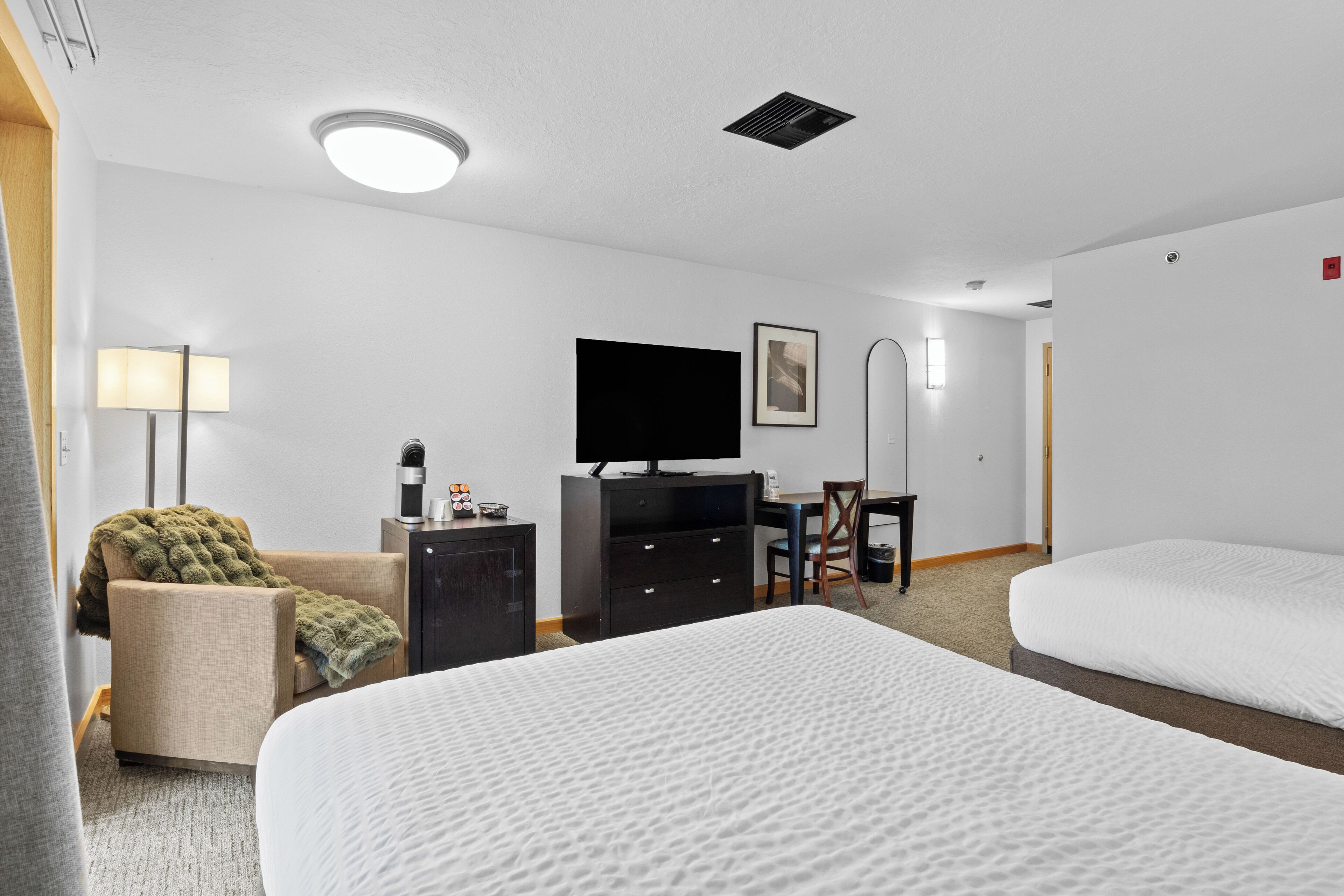 A hotel room with two beds, a desk, a chair, a television, and a lamp.