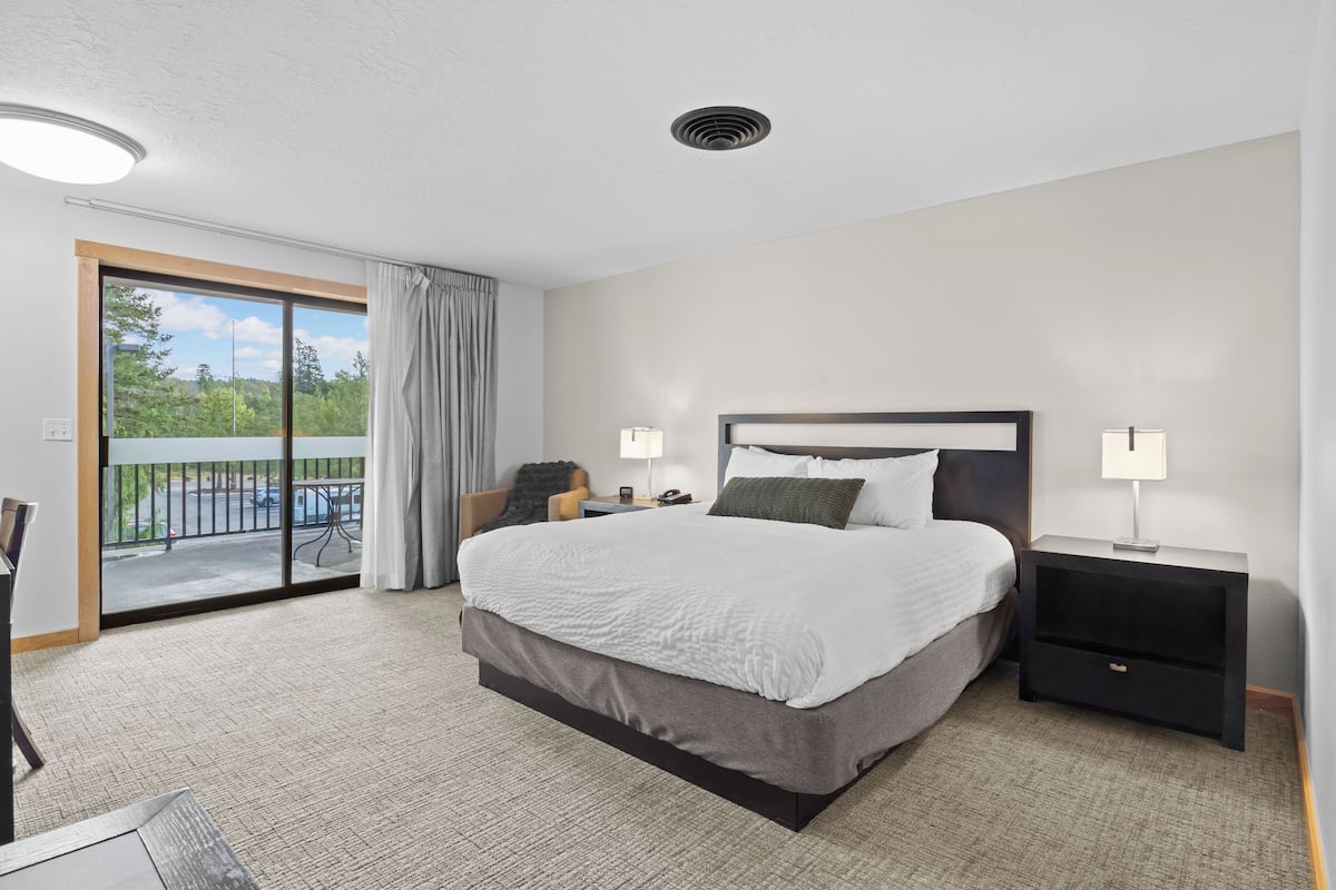 Une chambre d’hôtel moderne, dotée d’un grand lit, d’une table de chevet, d’un bureau et offrant une vue sur l’extérieur.