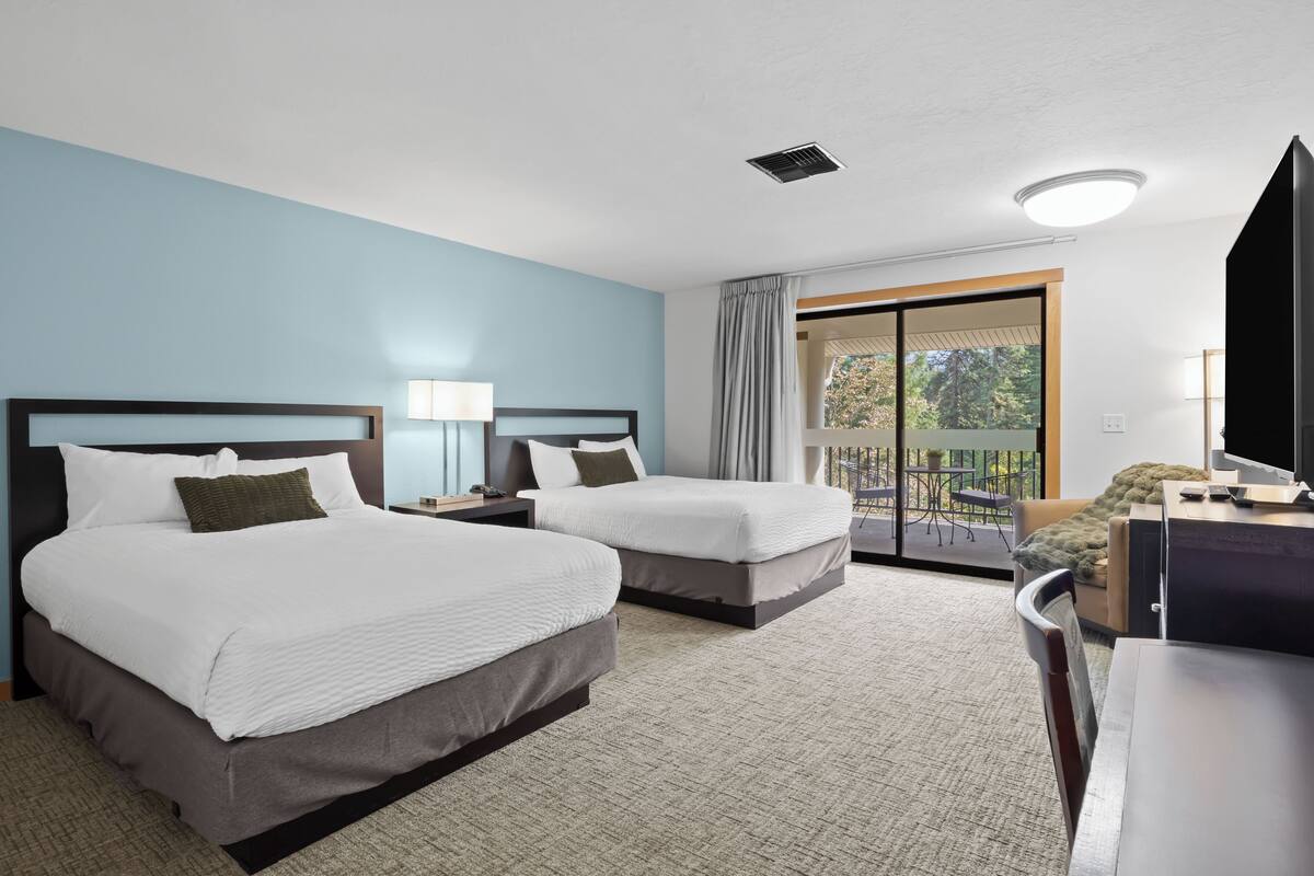 Une chambre d’hôtel avec deux lits, un bureau, une chaise, une télévision et un balcon donnant sur la verdure.