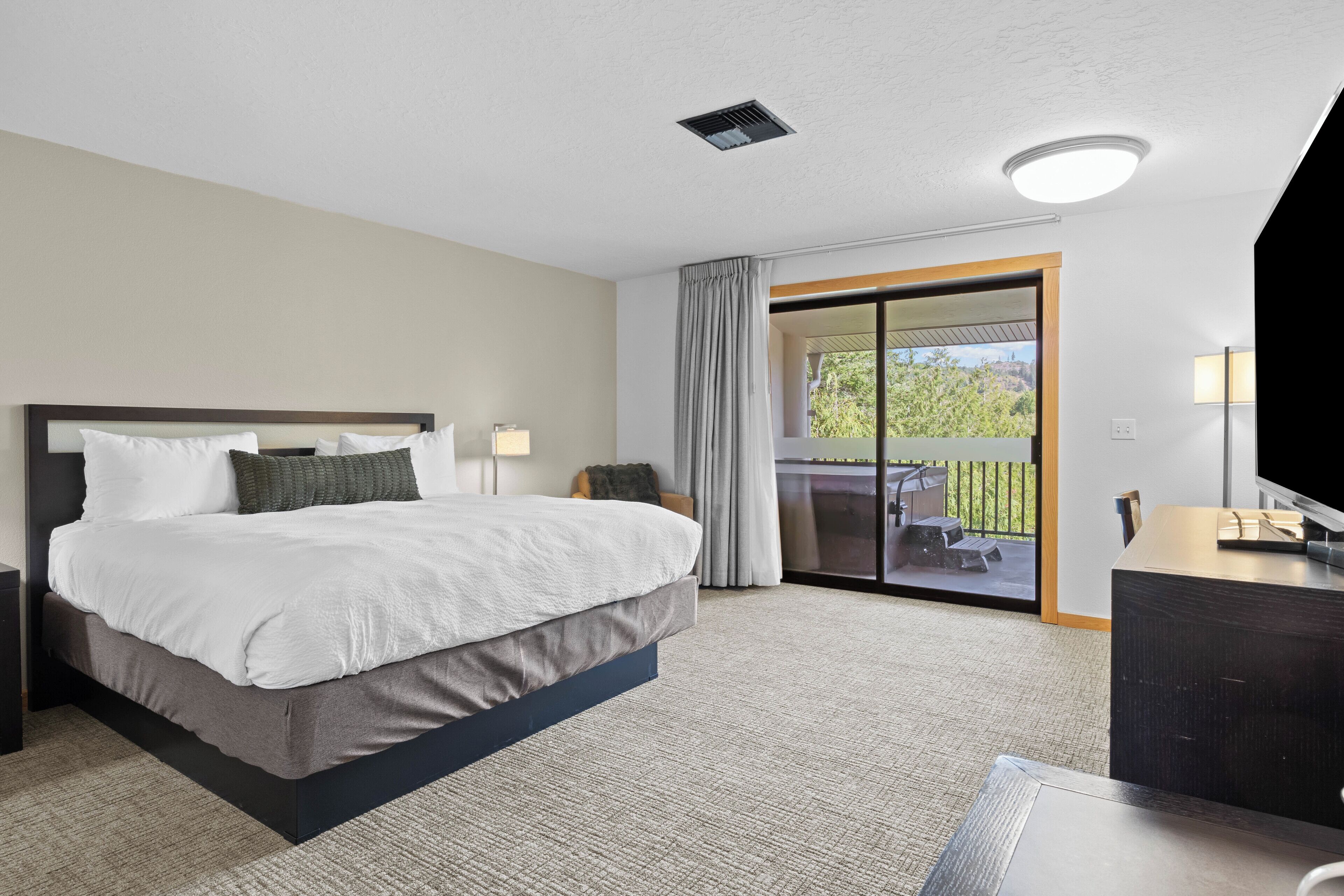 A hotel room with a bed, a desk, a TV, a balcony with a view, and a sliding door.