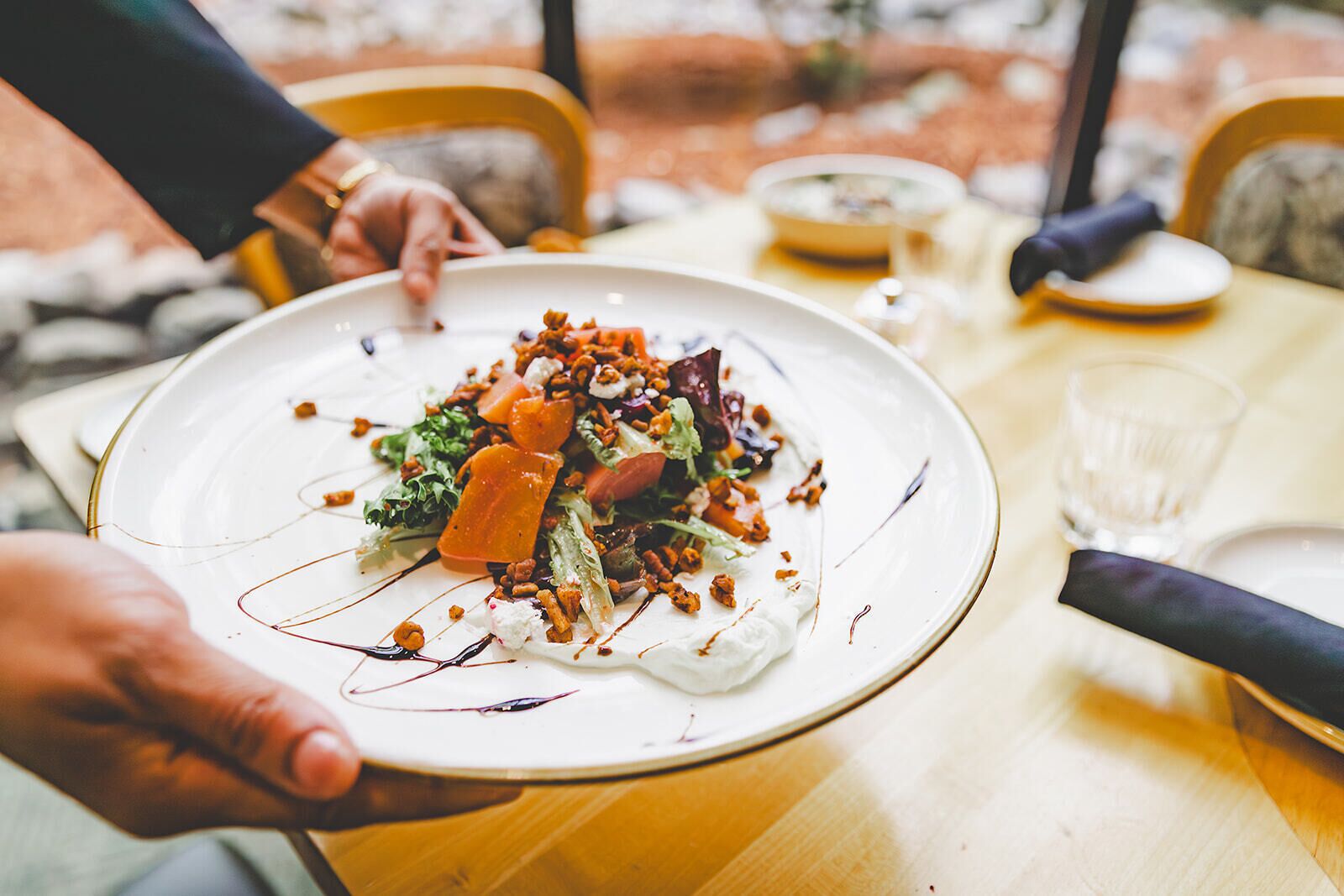 A person holding a plate with a salad on a wooden table.