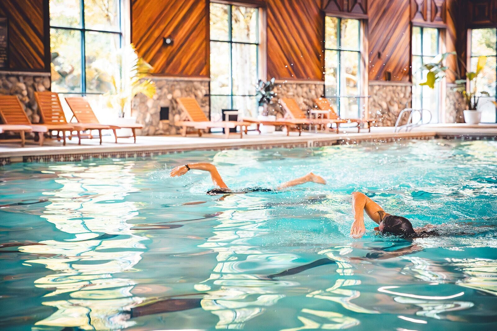 Une piscine à l’eau claire, des chaises longues en bois et un mur de pierre en arrière-plan.