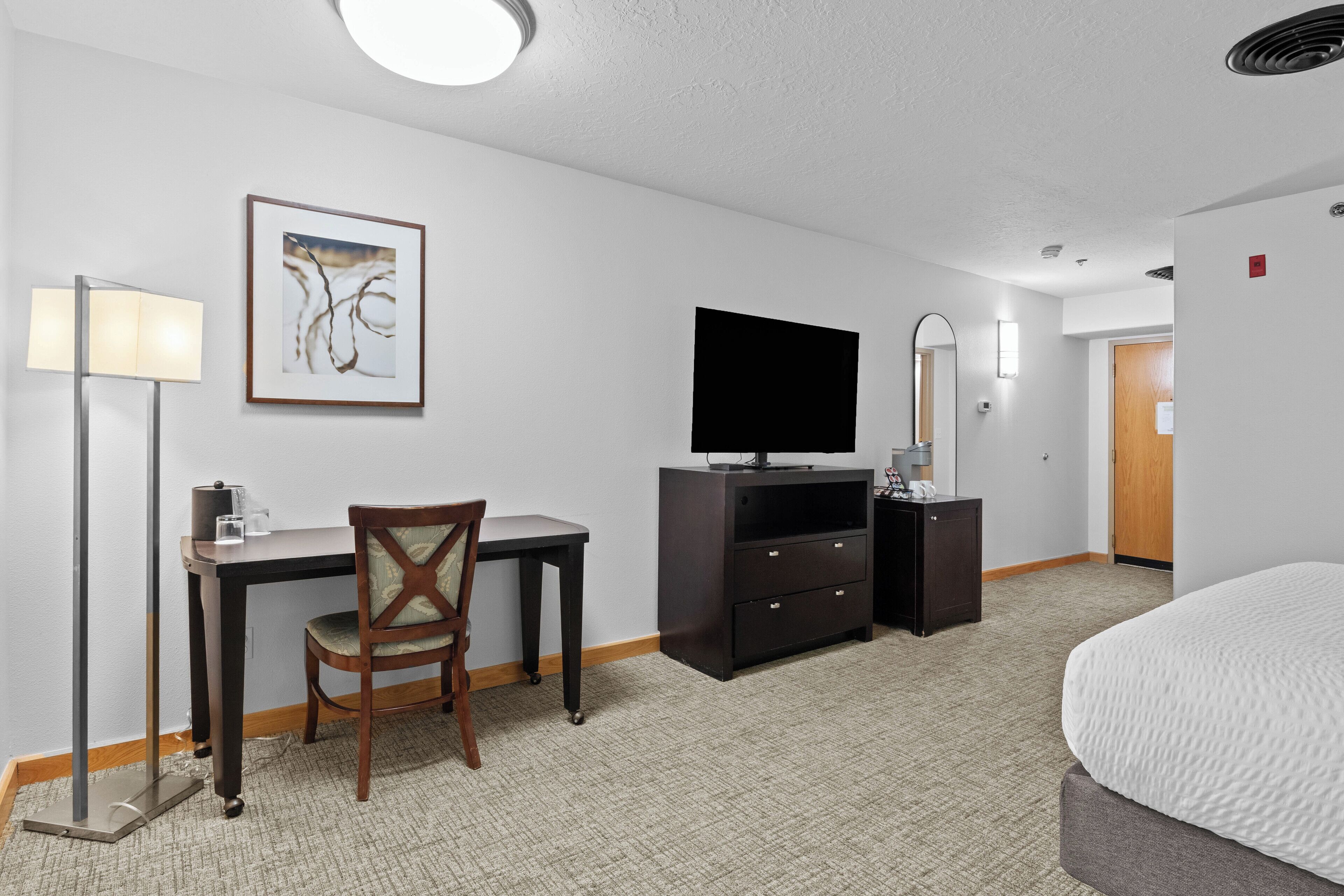 Habitación de hotel con cama, escritorio, silla, televisión y un cuadro en la pared.