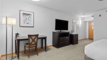 Habitación de hotel con cama, escritorio, silla, televisión y un cuadro en la pared.