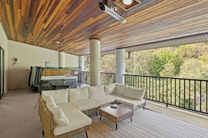 A covered outdoor seating area with a wooden ceiling, a white sofa, and a table.