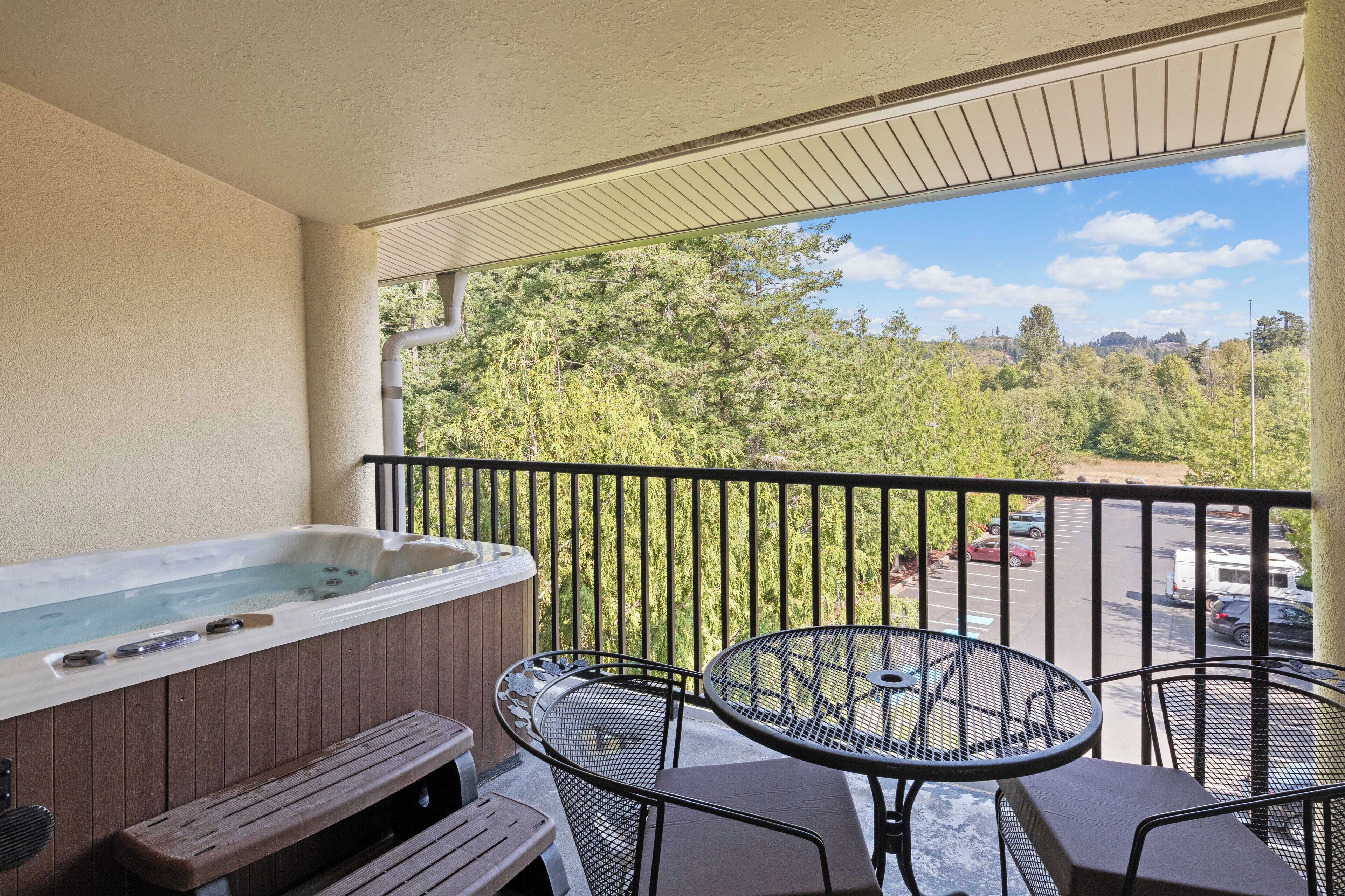 A balcony with a hot tub, two metal chairs, and a wooden bench.