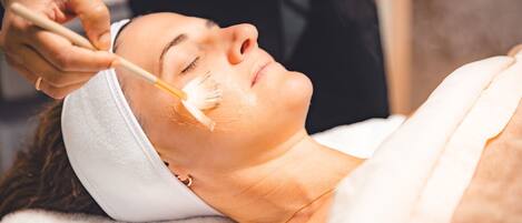 A person lying down with a headband, receiving a facial treatment.