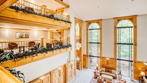 Interior de un hotel con varios niveles, paneles de madera, una escalera y un área de descanso con vistas al exterior.