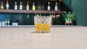 A bar area with a glass of amber-colored liquor, shelves with various bottles, and a potted plant.