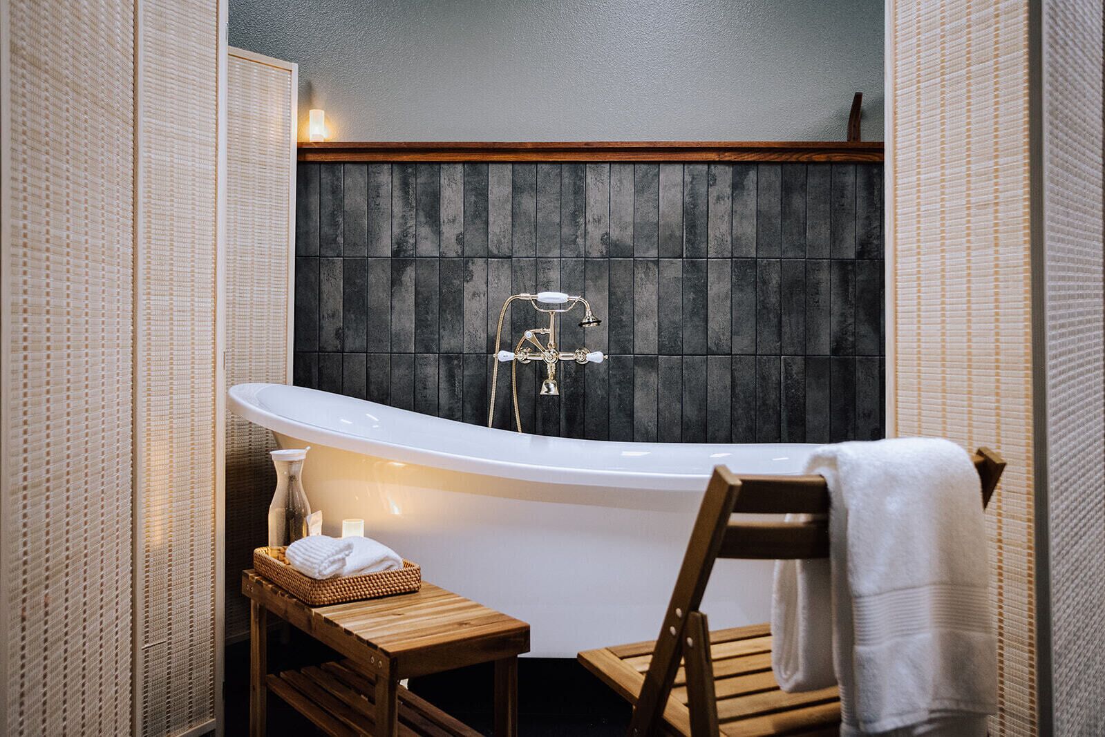 Un baño moderno con una bañera independiente, un banco de madera y una pared con textura.