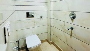 Une petite salle de bain carrelée, équipée de toilettes, d’une douche et d’un miroir.