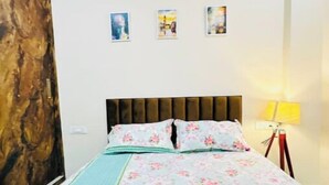 Une chambre à coucher avec un lit, une tête de lit en bois, une table de chevet avec une lampe, et trois tableaux encadrés accrochés au mur.