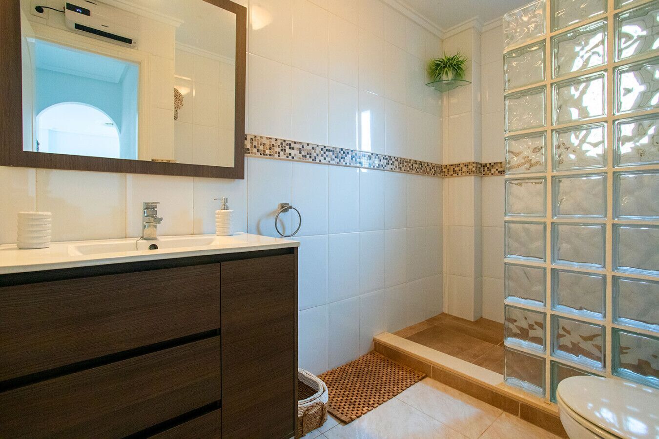 A bathroom with a white sink, dark wooden vanity, a glass shower enclosure, and a tiled floor.