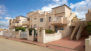 A multi-story residential building with balconies, a gated entrance, and a staircase leading to the upper floors.