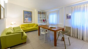 A bright living room with a yellow sofa, a wooden dining table, and a bookshelf. - Apartments Florence-San Lorenzo Market (Florence)