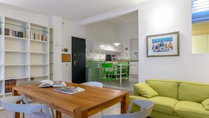 A modern living room with a wooden dining table, white chairs, a green sofa, and a bookshelf. - Apartments Florence-San Lorenzo Market (Florence)