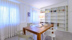 A dining area with a wooden table, white chairs, a bookshelf, and a lamp. - Apartments Florence-San Lorenzo Market (Florence)