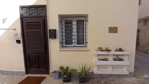 Un bâtiment doté d’une porte en bois sombre, d’une fenêtre avec des barreaux en métal et d’un jardinier blanc contenant des plantes.