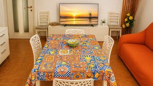 Un coin repas avec une table recouverte de carreaux colorés, un téléviseur diffusant une scène de coucher de soleil et un canapé à l’arrière-plan.