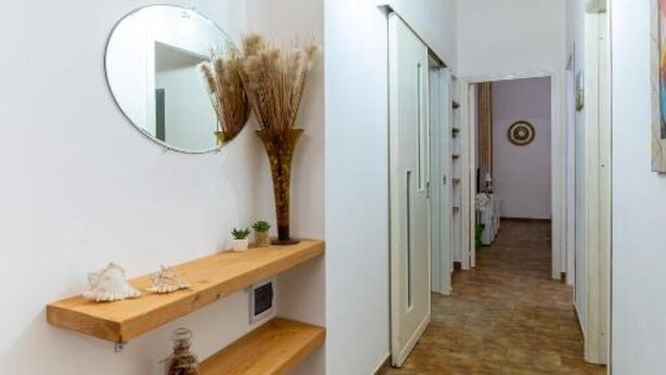 Un couloir avec une étagère en bois, un miroir et un vase contenant des plantes séchées.
