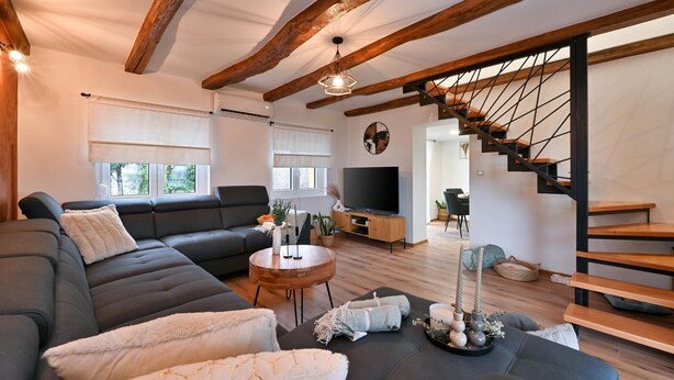 A modern living room with a dark grey sofa, a round wooden coffee table, and a staircase with wooden railings.