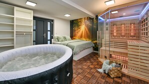 A modern spa room with a hot tub, a sauna, and a bed with a forest-themed wall mural.