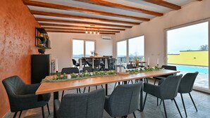 A dining area with a long wooden table, six chairs, and a view of a swimming pool.