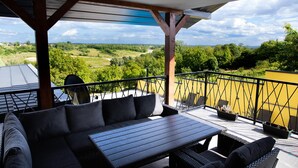 A covered outdoor seating area with a sofa and tables, overlooking a scenic landscape.