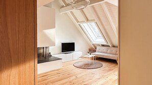 A modern loft-style living area with a high ceiling, wooden flooring, a sofa, a TV, and a small table. - VK - Zürich Airport - Luxury - Homestay  (Kloten)