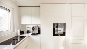 A modern kitchen with white cabinetry, a built-in oven, a coffee machine, and a window providing natural light. - VK - Zürich Airport - Luxury - Homestay  (Kloten)