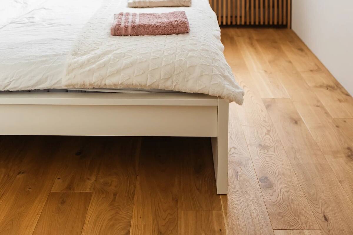 Un dormitorio con techo inclinado, una ventana, una cama con colchón y almohadas blancas, y suelo de madera.