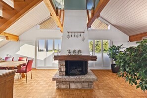 A spacious room with a stone fireplace, wooden beams, and large windows offering views of the outdoors. - VK - Zürich Airport - Luxury - Homestay  (Kloten)