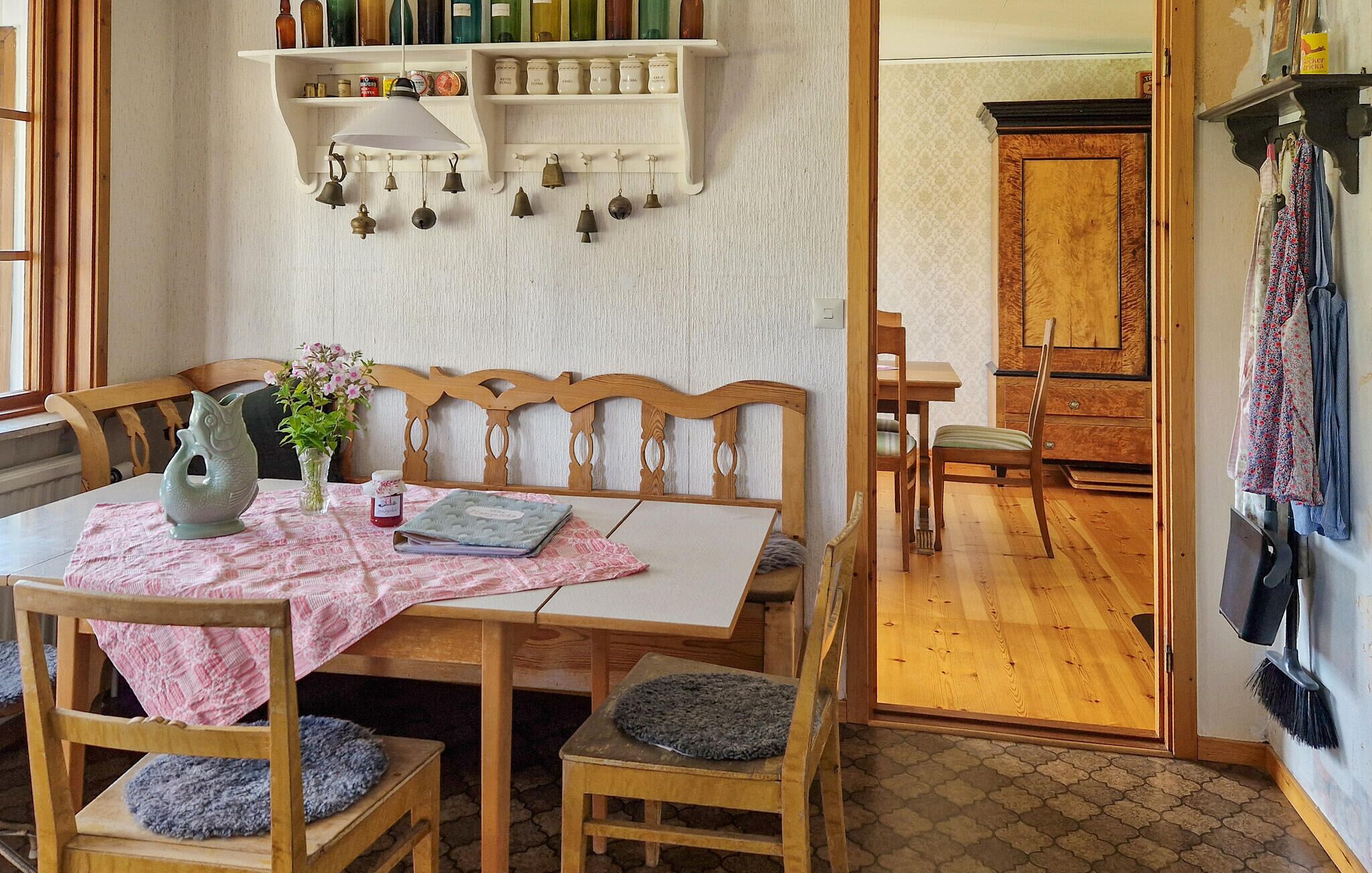 A dining area with a wooden table, chairs, a vase with flowers, and a hanging bell arrangement.