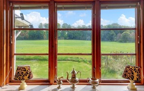 Una habitación con un amplio ventanal que ofrece vistas a un campo verde y árboles. Hay dos lámparas en el alféizar.