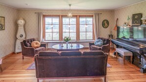 Ein Wohnzimmer mit einem Flügel, einer Uhr und einem großen Fenster mit Vorhängen.