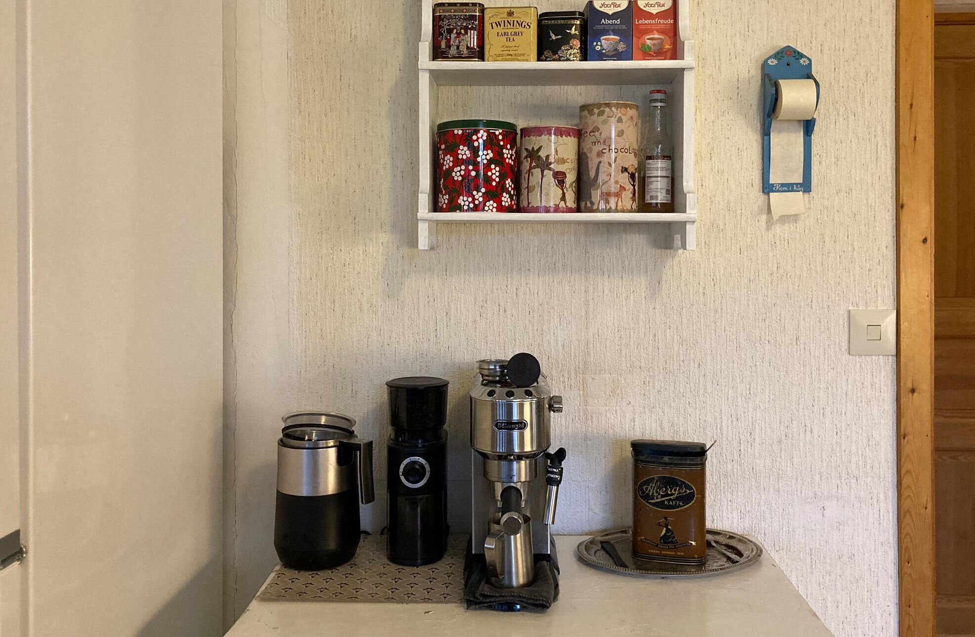 A kitchenette with a coffee machine, a kettle, and various tea and coffee tins on the wall.