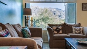 Un salón con dos sofás, una lámpara y vistas a las montañas a través de una ventana.