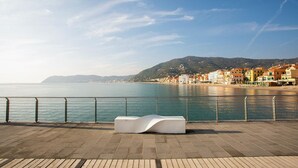 A waterfront promenade with a modern white bench, a metal railing, and a view of colorful buildings along the coast. - 1 bedroom amazing home in Onzo (Onzo)