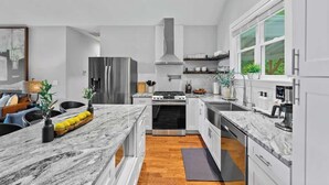 A modern kitchen with white cabinets, a stainless steel refrigerator, a gas stove, and a large window. - 5 mi. to Asheville•HotTub•Sauna•MtnViews•FirePit•PoolTable (Swannanoa)