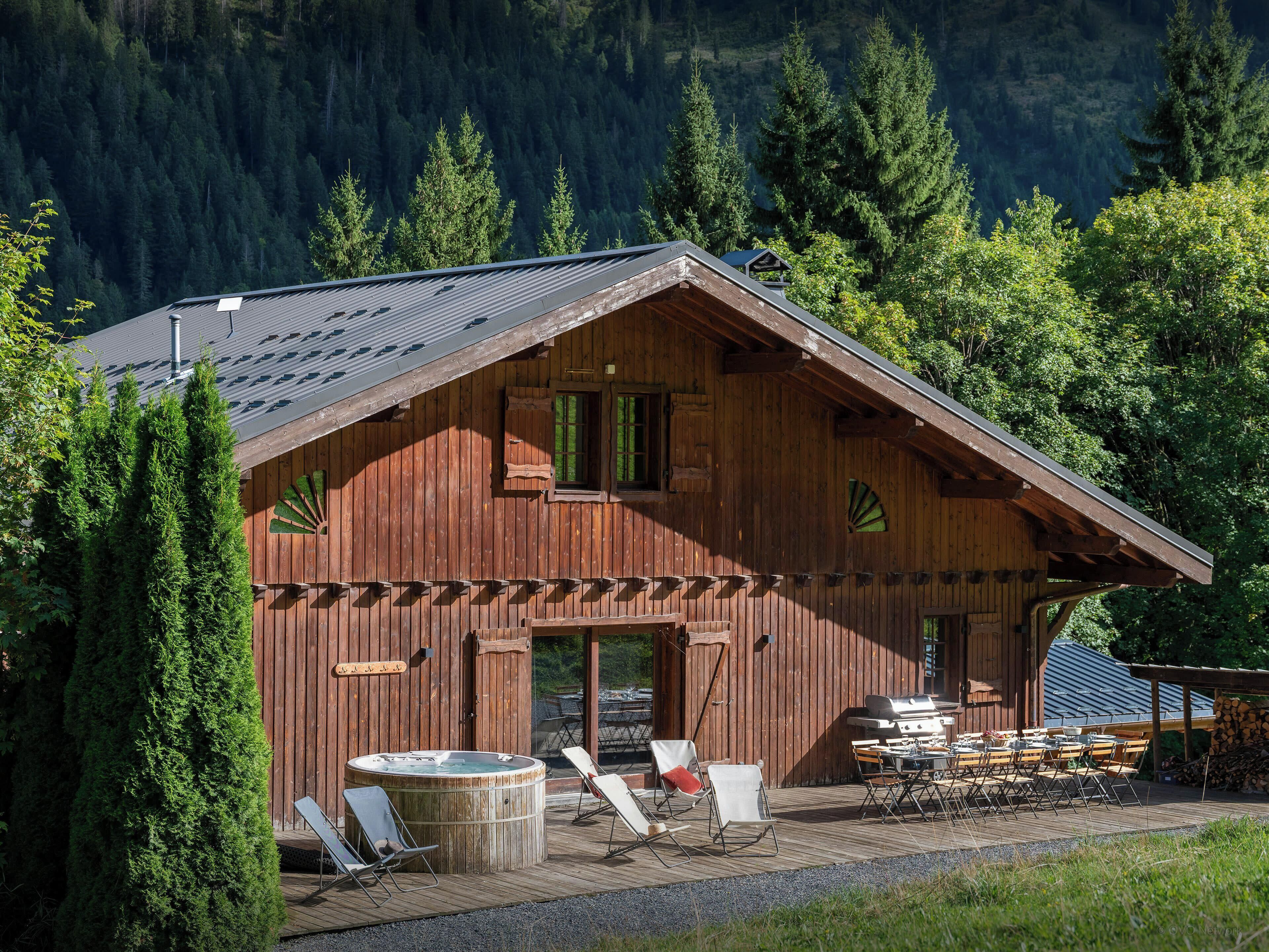 Une cabane en bois avec un toit en pente, un jacuzzi et un espace salon extérieur.