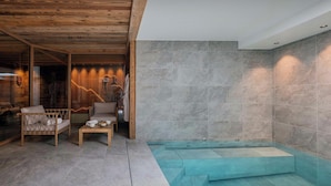 Un espace spa moderne doté d’un plafond en bois, d’un mur en pierre et d’un petit coin salon avec une table et des chaises.