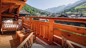 Une terrasse en bois avec une table et des chaises, d’où l’on a vue sur un village et des montagnes.