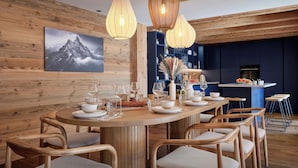 Une table de salle à manger en bois, dressée avec de l’argenterie blanche, des assiettes, des bols et des verres, entourée de chaises en osier.