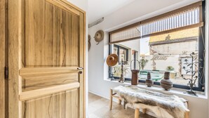 Una habitación con puerta de madera, un banco y una ventana con vistas a un jardín y un edificio.
